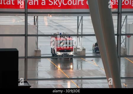 Flughafenfeuerwehrwagen auf einer nassen Landebahn, durch Terminalfenster gesehen, der Rettungsdienste an einem regnerischen Tag auf dem Flugplatz vorstellt Stockfoto