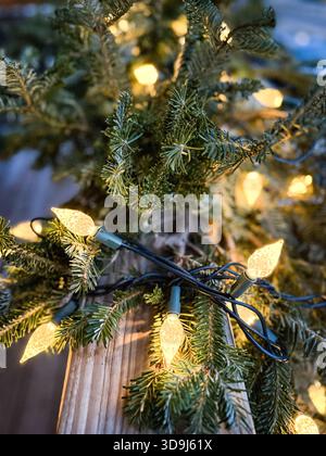 Eine Reihe von warmen Weihnachtslichtern beleuchtet die natürliche immergrüne Zweiggirlande in der kalten Winterszene. Stockfoto
