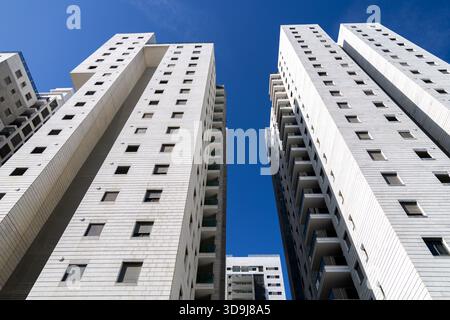 Flacher Blick auf neu gebaute moderne Wohnhochhäuser mit heller Steinverkleidung und Glasbalkonen vor klarem blauem Himmel in einem modernen Stadtviertel Stockfoto
