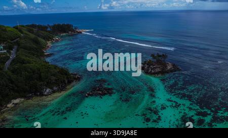 Tropisches Meer mit leuchtenden türkisfarbenen Riffen, Rocky Islet und üppiger grüner Küstenlandschaft Stockfoto