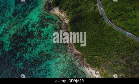 Tropical Coastal Road durch dichten Wald, Rocky Shoreline und türkisfarbenes Flachriff Stockfoto