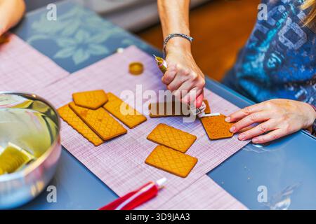 Nahaufnahme einer Frau, die beim Zusammenbau des Weihnachtskekshauses auf Lebkuchenstücke Glasur aufträgt. Schweden. Stockfoto