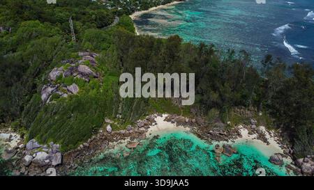Tropische Landzunge mit üppigem Wald, Granitfelsen, abgelegenem Strand und ausgedehntem Turquoise Reef System Stockfoto