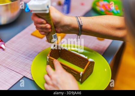 Nahaufnahme einer Frau, die während der Montage Weiße Glasur auf Lebkuchenhauswänden auf Grünplatte aufträgt. Schweden. Stockfoto