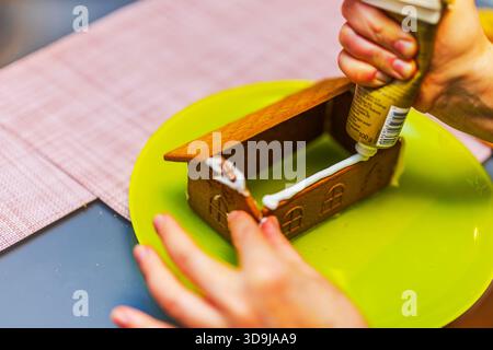 Frau, die ein Lebkuchenhaus auf einem Teller zusammensetzt, während sie weiße Glasur aufträgt, um die Kekswände zusammenzuhalten. Schweden. Stockfoto
