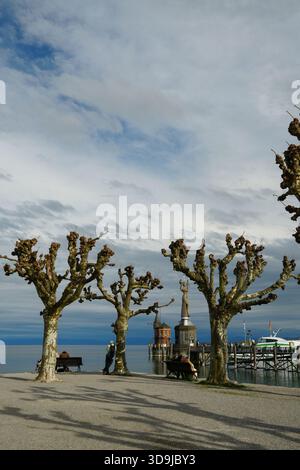 Malerischer Blick auf die Hafenpromenade Konstanz mit großen geschnittenen Platanen, die die Imperia-Statue und den historischen Pegelhäuschen-Turm am Co-See umrahmen Stockfoto