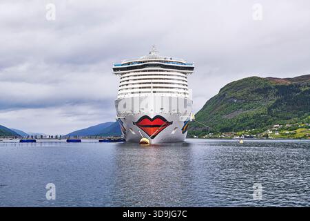Das Kreuzfahrtschiff AIDAnova liegt in einem ruhigen norwegischen Fjord, dessen farbenfrohe Bugkunstwerke und hoch aufragende Decks sich von grünen Hängen und einem Clos abheben Stockfoto