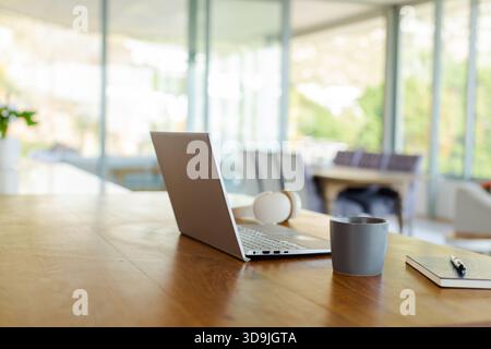 Laptop-Computer auf Holzschreibtisch mit Kopfhörern, Kaffeetasse, Notebook und Stift in der Nähe von Fenstern Stockfoto