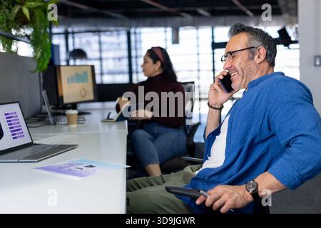 Verschiedene Kollegen, die über ein Smartphone sprechen, arbeiten an einem Laptop in modernen Büros mit Karten und Kopierraum Stockfoto