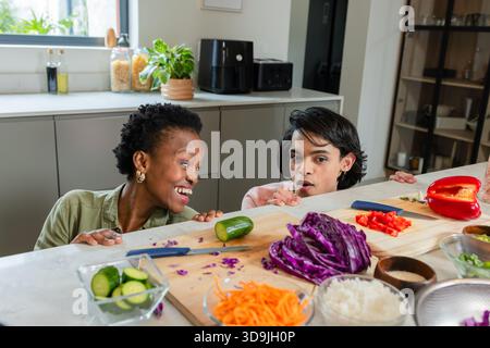 Verschiedene Freunde lehnen sich über die Küchenzeile und schauen auf gehacktes Gemüse auf hölzernem Schneidebrett Stockfoto