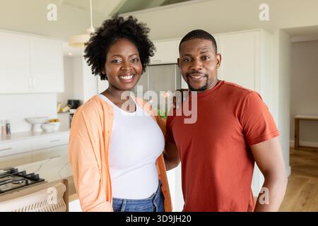 Afroamerikanisches Paar, das sich in der modernen Küche am Kochfeld und Kühlschrank umgibt und lächelt Stockfoto