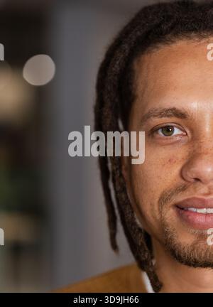 Die rechte Hälfte des männlichen Gesichtes macht Augenkontakt und lächelt im Studio, Dreadlocks, senfbraune Oberseite Stockfoto
