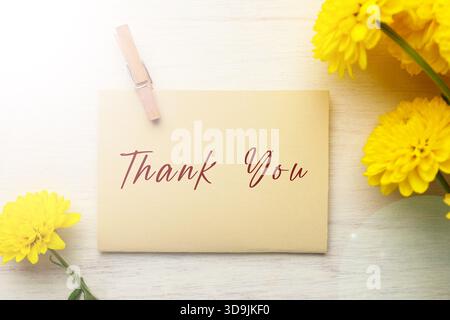 Dankeskarte mit Umschlag und Blumen auf weißem Holztisch, Blick von oben Stockfoto