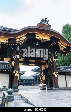 Ein kunstvoll verziertes Tempeltor in Kyoto verfügt über geschwungene, dunkle Holztraufe mit komplizierten Goldakzenten, die in das feierliche Tempelgelände führen. Stockfoto