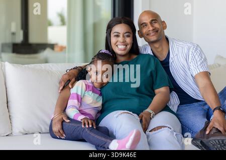 Afroamerikanische Familie auf weißem Sofa im Wohnzimmer mit Glasschiebetür und Kissen Stockfoto