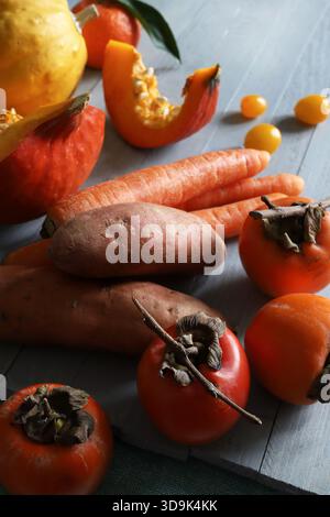 Eine Vielzahl von frischen gelben und orangen Herbstprodukten wie Kürbisse, Persimmons, Karotten und Süßkartoffeln auf einem grauen Holztisch. Gesunde Ernährung. Stockfoto