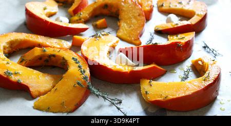 Kürbisscheiben, gewürzt mit frischem Thymian und nativem Olivenöl extra in einem Blech, fertig zum Backen. Eine Winterbeilage. Gesunde und vegetarische Lebensmittel. Stockfoto