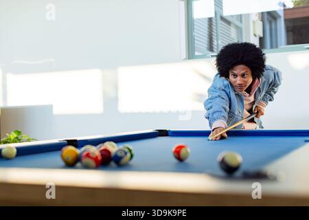 Afroamerikaner, der mit dem Stichstock auf Bälle auf dem Billardtisch zu Hause zielt, Kopierraum Stockfoto