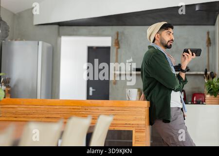 Indischer Mann lehnt sich gegen den Tresen im Café und spricht in das Smartphone neben dem weißen Becher, Kopierraum Stockfoto