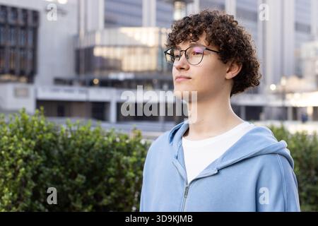 Mann, der in der Nähe grüner Sträucher im Bürogebäude stand, mit runder Brille und Hoodie, Kopierraum Stockfoto