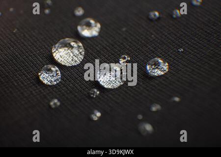 Wassertropfen liegen auf einer dunklen, strukturierten Stoffoberfläche Stockfoto