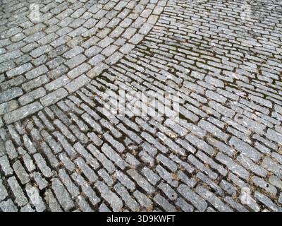 Altmodischer Kopfsteinpflasterweg Hintergrund, graue Granit Pflastersteine mit einem Eckmuster, nasse Textur, Landschaft Pflasterweg Baubestand Stockfoto