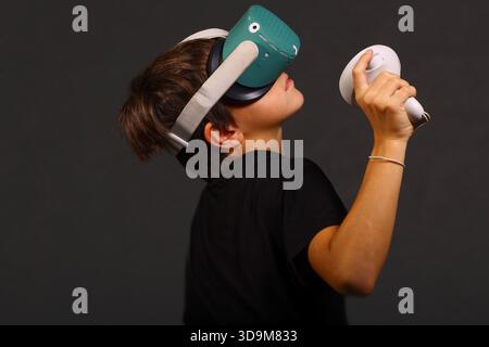 Junge mit VR-Headset, der den Controller während einer immersiven Gaming-Session nach oben hält, moderne interaktive Technologie. Stockfoto