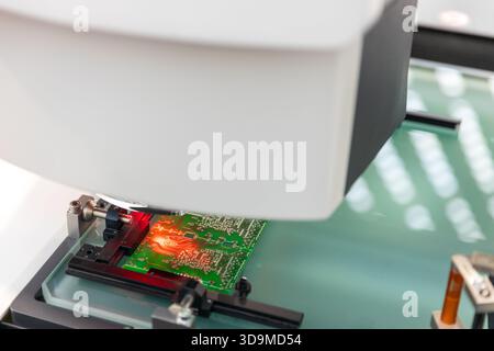 Nahaufnahme einer automatischen optischen Inspektionsmaschine (AOI), die eine grüne Leiterplatte (PCB) während des Qualitätskontrollprozesses auf Fehler untersucht Stockfoto