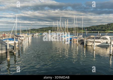 Friedliche Marina Szene in Oehningen am Bodensee auf der Halbinsel Hoeri in Baden-Württemberg. Unter einem teilweise bewölkten Himmel liegen Motorboote und Segelboote an einem Steg. Die sanften Hügel des Thurgau in der Schweiz sind im Hintergrund zu sehen. Stockfoto