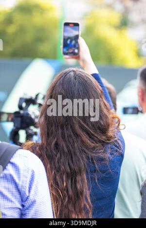 Eine Frau in einer Menschenmenge hält einen unvergesslichen Moment auf ihrem Smartphone fest, teilt das Erlebnis mit und erstellt digitale Inhalte für soziale Medien und Online-Plat Stockfoto