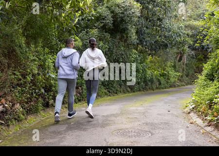 Verschiedene Paare tragen Hoodies, Leggings und Laufschuhe beim Joggen auf gepflasterten Wanderwegen durch den Wald Stockfoto