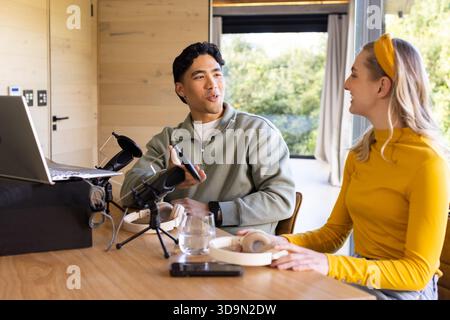 Verschiedene Co-Moderatoren und Freunde nehmen Podcasts im Heimstudio mit Laptop-Kondensatormikrofon auf Stockfoto