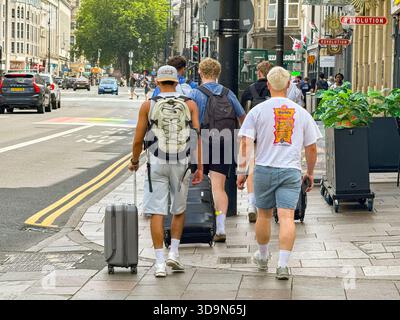 Cardiff, Wales, Vereinigtes Königreich - 20. Juni 2025: Rückansicht einer Gruppe junger männlicher Besucher von Cardiff, die Koffer entlang einer Straße im Stadtzentrum fahren Stockfoto