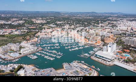 Aus der Vogelperspektive des Jachthafens von Vilamoura in Portugal mit zahlreichen Booten, die im Wasser angedockt sind, und Gebäuden entlang der Küste unter einem klaren blauen Himmel. Antenne Stockfoto