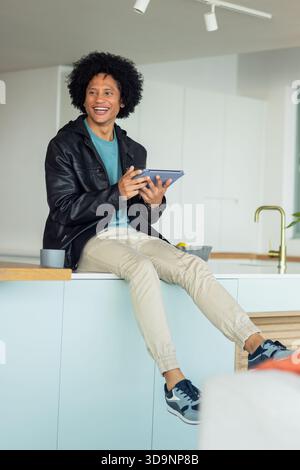 Afroamerikaner, der auf der Kücheninsel sitzt und ein Tablett neben einer Tasse und einer Schüssel Zitronen hält Stockfoto