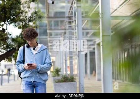 Mann, der auf einem überdachten Gehweg mit Hoodie und Kopfhörern läuft, während er Smartphone und Kopierraum überprüft Stockfoto