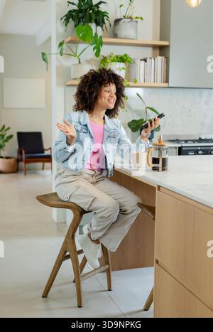 Afroamerikanische Frau, die mit Smartphone und Fernbedienung auf der Marmorinsel Gesten mit französischer Presse macht Stockfoto