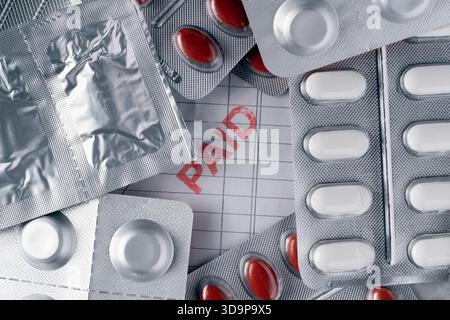 Ein Haufen Pillen mit einem roten Wort auf einem Blatt Papier. Die Pillen sind überall auf dem Papier verstreut und das Wort bezahlt steht in der Mitte. Sce Stockfoto