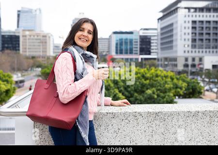Reife Erwachsene Frau, die sich an das Geländer lehnt und eine Kaffeetasse auf dem Blick der Stadt hält, Kopierraum Stockfoto