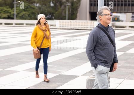 Seniorenpaar schlendern auf dem plaza in der Nähe des Bürogebäudes mit Tragetasche, Umhängetasche, Kopierraum Stockfoto