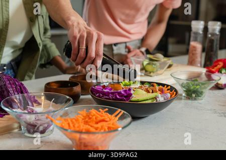 Zwei Köche gießen Dressing in eine schwarze Salatschale auf einer Steinplatte in der Nähe von Glasschalen Stockfoto