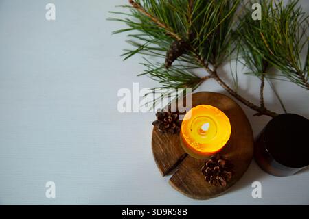 Brennendes Kerzenfeuer auf einem hölzernen Kerzenleuchter in der Nähe von grünem Tannenzweig. Großaufnahmehintergrund-Design-Konzept mit weißem leer Stockfoto