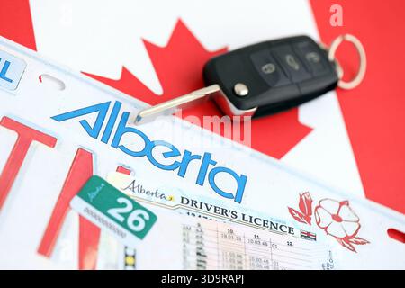 Alberta canadian Autokennzeichen und Zündschlüssel auf der Flagge von Kanada Nahaufnahme. Führerschein- und Zulassungskonzept Stockfoto