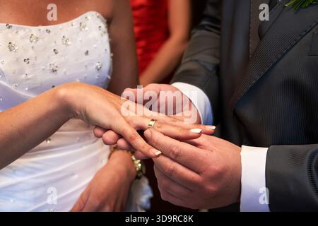 Nahaufnahme eines Bräutigams, der während der Zeremonie einen goldenen Ehering auf den Finger der Braut legt, symbolisiert Liebe, Engagement und den Beginn ihrer Hochzeit Stockfoto