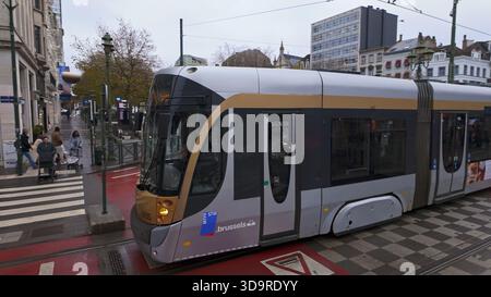 BRÜSSEL, BELGIEN - 26. NOVEMBER 2025 - Moderne Straßenbahnfahrt auf Gleisen entlang Fußgängern, die auf einer nassen Stadtstraße in Brüssel, Belgien, spazieren Stockfoto