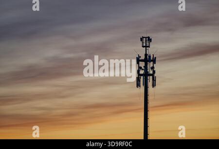 Ein Funkturm für LTE UMTS und mobiles Internet in Hamburg bei Sonnenuntergang vor goldener und blaugrauer Kulisse. Kabel hängen von den Antennen. Stockfoto