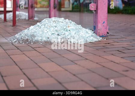 Ein Haufen zersplitterter Glassplitter auf einem Backsteinpflaster in der Nähe einer farbenfrohen Graffiti-Wand, der urbanen Verfall und Vernachlässigung zum Ausdruck bringt. Stockfoto