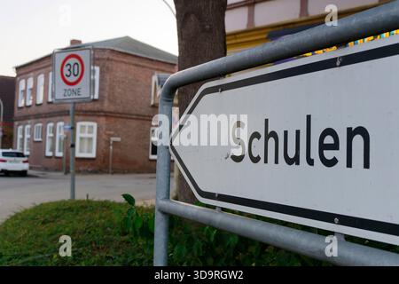 Ein weißer Pfeil auf Metallpfählen zeigt links mit deutschem Schulschild. Im Hintergrund zeigt ein Verkehrsschild Zone 30 an, das eine Geschwindigkeitsbegrenzung von 30 km h anzeigt Stockfoto