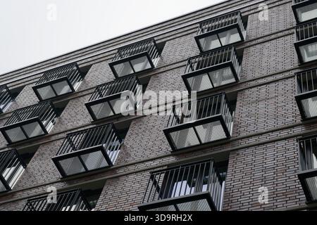 Mehrstöckiges Wohngebäude aus weißem Backstein mit zahlreichen identischen rechteckigen Balkonen mit Metallstangengeländern, die eine einheitliche Box schaffen Stockfoto