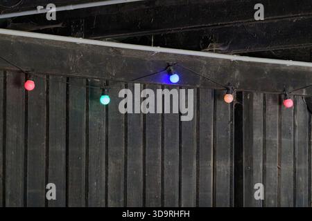 Ein staubiges altes Holzgebäude mit rostigen Metallbalken trägt eine bunte Lichterkette, die von den Nägeln hängt. Dicke Spinnennetze bedecken die Oberseite, wodurch ein entsteht Stockfoto